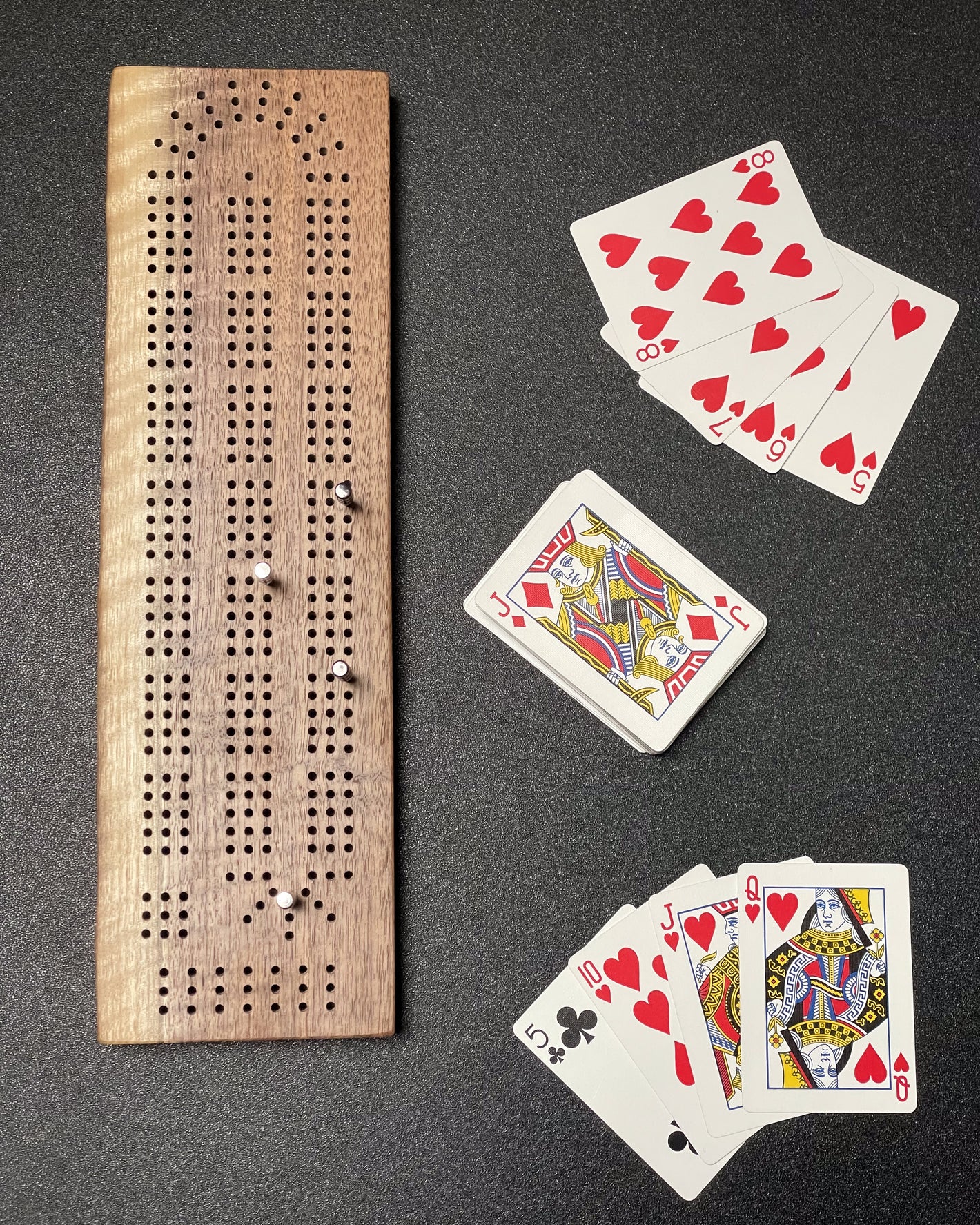 A table with a dark walnut wooden cribbage board and a deck of cards.