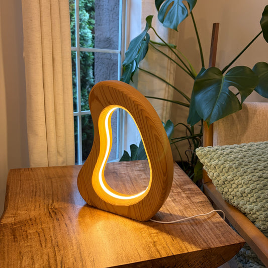 Wooden lamp with a glowing interior on a wooden surface next to a plant