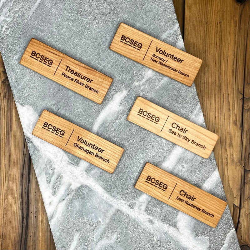 Set of wooden nameplates with BCSEG branding on a stone surface