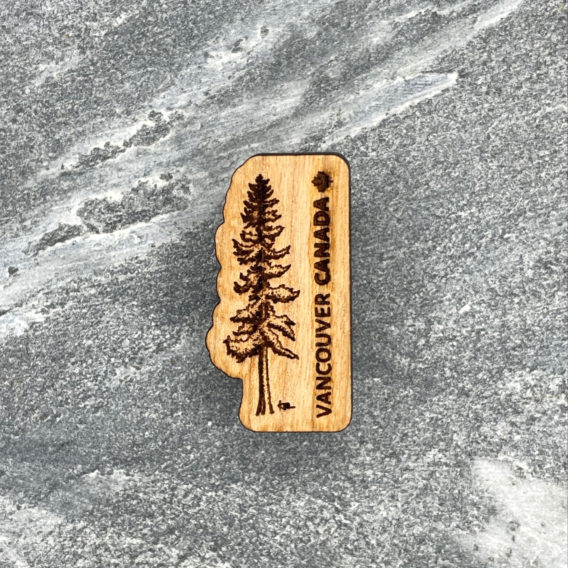 Wooden souvenir magnet with a tree design and 'Vancouver Canada' text on a stone surface